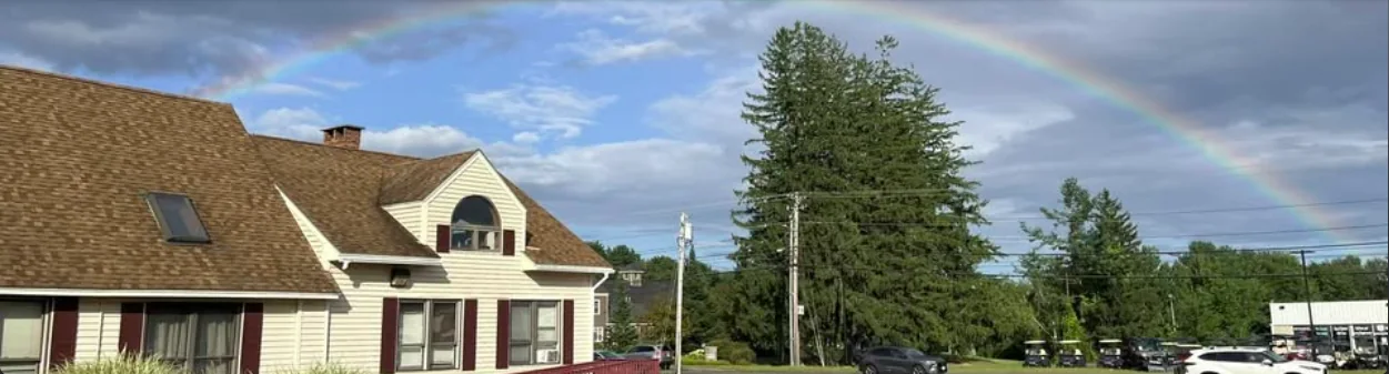 The cream clapboard building at 890 Portland Road in Saco, photographed from the parking lot under a rainbow.